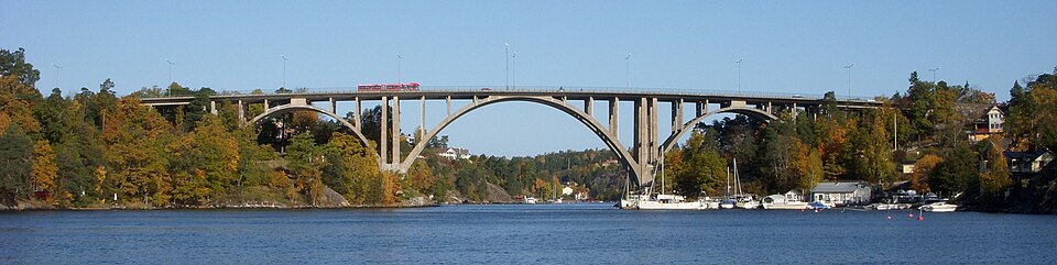 Skurubron i Nacka. En buss passerar över bron. Båtar ligger vid vattnet nedanför.